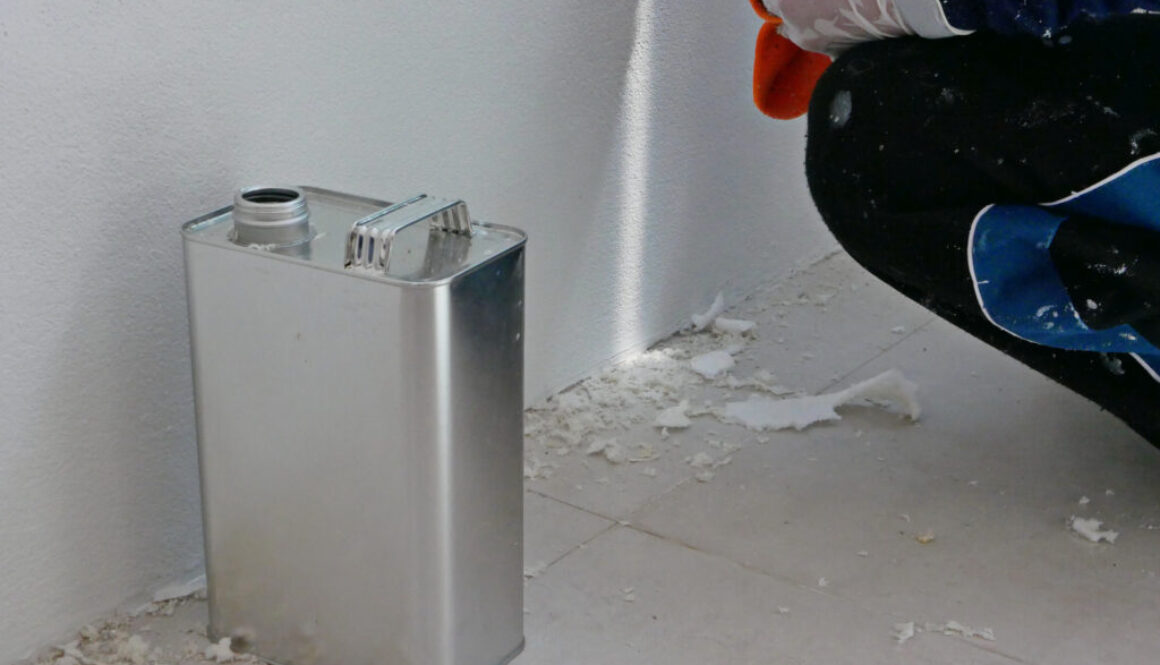 A gallon of thinner placed next to old concrete wall, while a painter is removing sticky rough glue and tape remain on the wall, as a preparation before starting the paint the house